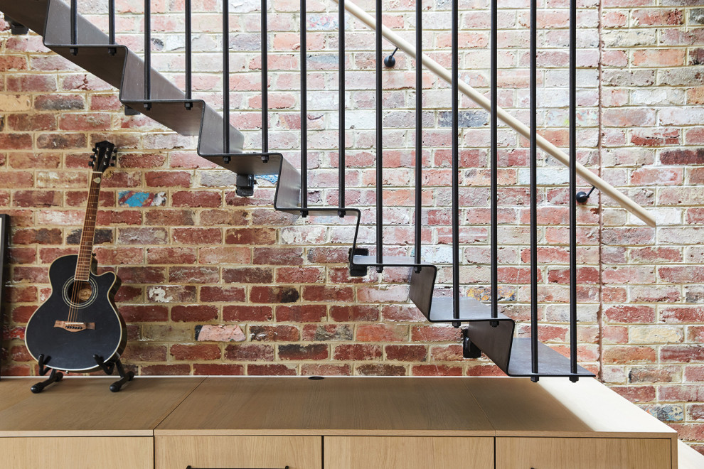 メルボルンにある中くらいなインダストリアルスタイルのおしゃれなかね折れ階段 (金属の蹴込み板、木材の手すり、レンガ壁) の写真