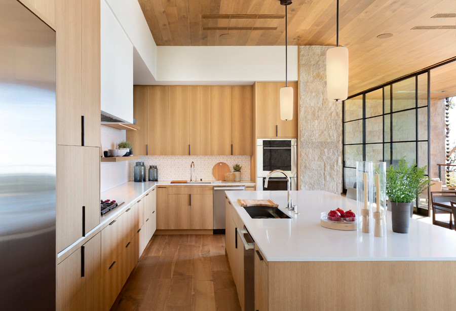 Medium sized modern l-shaped kitchen/diner in Los Angeles with a submerged sink, flat-panel cabinets, light wood cabinets, engineered stone countertops, white splashback, mosaic tiled splashback, integrated appliances, light hardwood flooring, an island, white worktops and a wood ceiling.