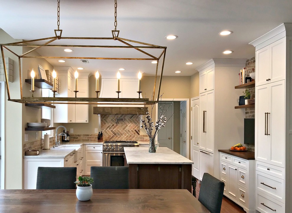 Photo of a mid-sized country l-shaped eat-in kitchen in Philadelphia with a farmhouse sink, shaker cabinets, white cabinets, granite benchtops, red splashback, brick splashback, panelled appliances, medium hardwood floors, with island, brown floor and grey benchtop.