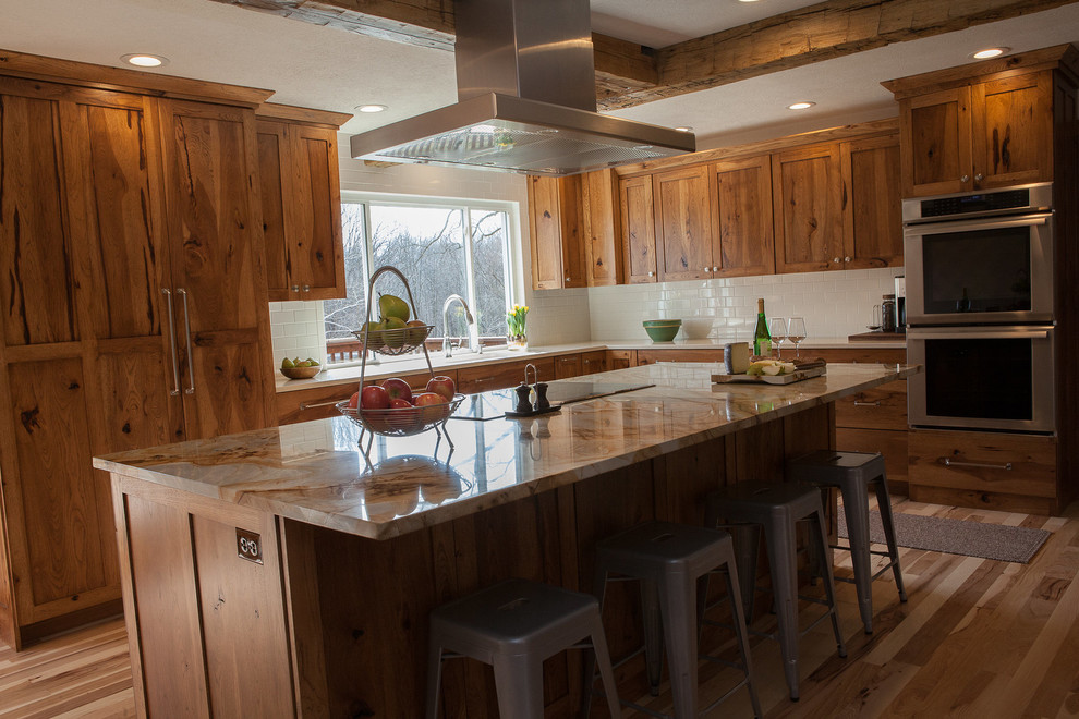Inspiration for a mid-sized country l-shaped eat-in kitchen in Indianapolis with an undermount sink, flat-panel cabinets, medium wood cabinets, quartzite benchtops, white splashback, ceramic splashback, panelled appliances, light hardwood floors, with island and multi-coloured benchtop.