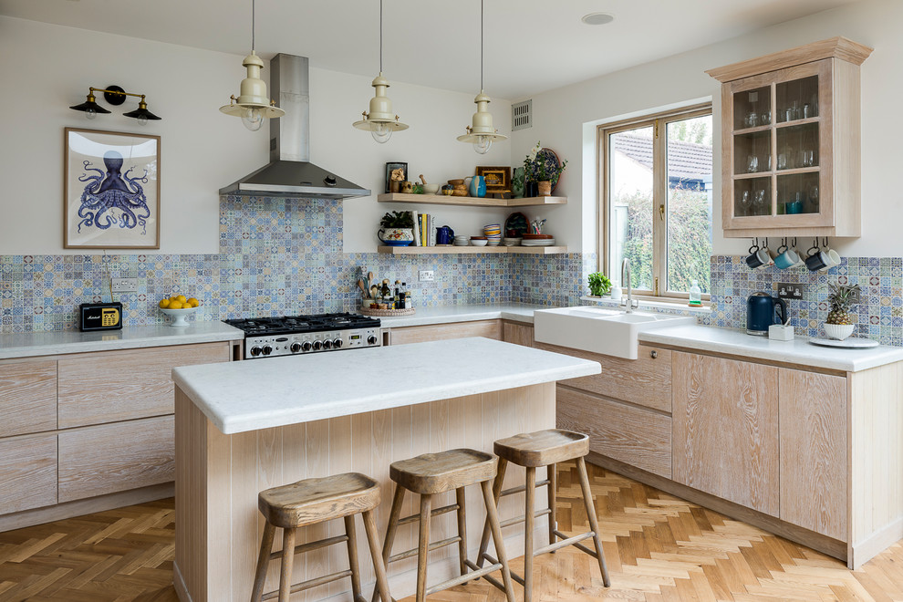 Inspiration for a beach style l-shaped kitchen in London with a farmhouse sink, flat-panel cabinets, light wood cabinets, multi-coloured splashback, ceramic splashback, light hardwood floors, with island and beige floor.