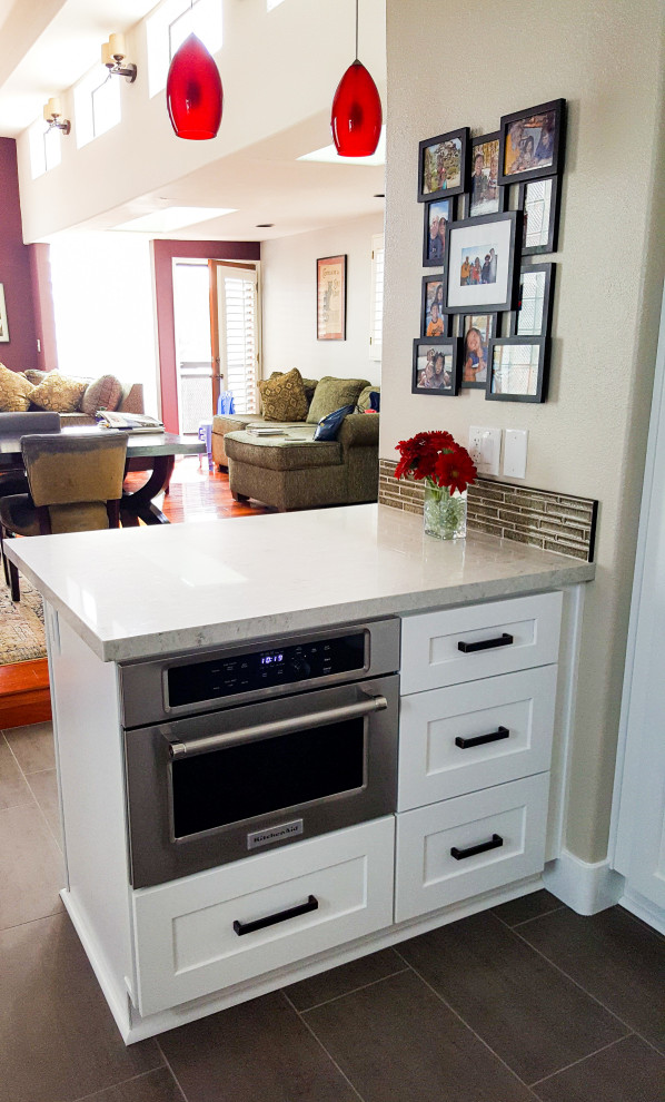 Inredning av ett modernt avskilt, litet vit vitt u-kök, med en undermonterad diskho, luckor med infälld panel, vita skåp, bänkskiva i kvarts, brunt stänkskydd, stänkskydd i glaskakel, rostfria vitvaror, klinkergolv i porslin, en halv köksö och grått golv