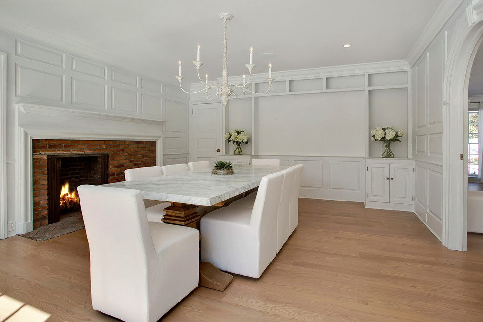 Photo of a large transitional separate dining room in New York with white walls, light hardwood floors, a standard fireplace, a brick fireplace surround and brown floor.