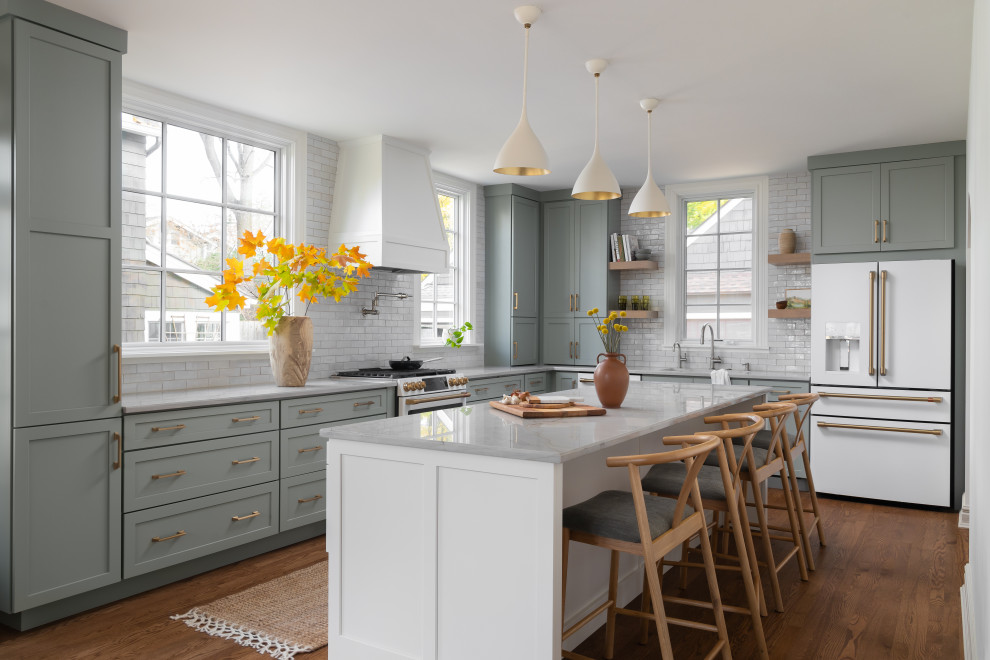 Inspiration for a large transitional l-shaped eat-in kitchen in Detroit with an undermount sink, shaker cabinets, grey cabinets, quartzite benchtops, white splashback, ceramic splashback, white appliances, medium hardwood floors, with island and grey benchtop.