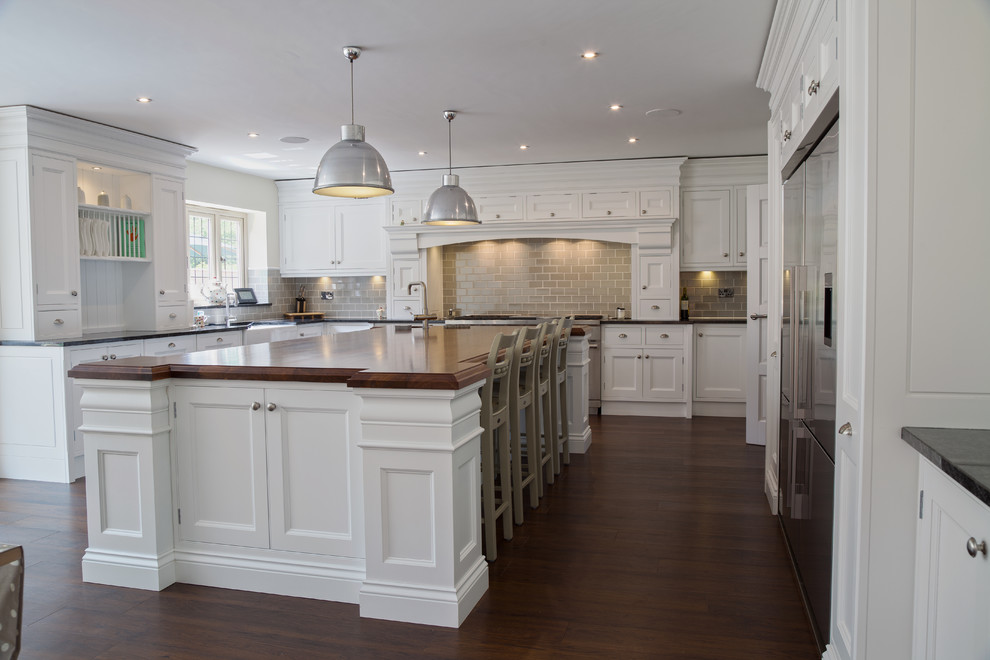 This is an example of a large traditional kitchen in Essex with a farmhouse sink, recessed-panel cabinets, white cabinets, grey splashback, subway tile splashback, stainless steel appliances, dark hardwood floors and with island.