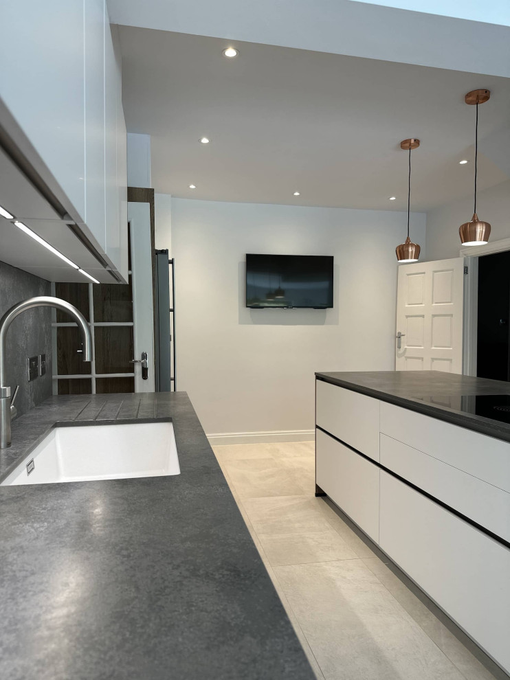 Inredning av ett skandinaviskt stort grå grått kök, med en integrerad diskho, släta luckor, vita skåp, bänkskiva i kvartsit, svarta vitvaror, en köksö och grått golv