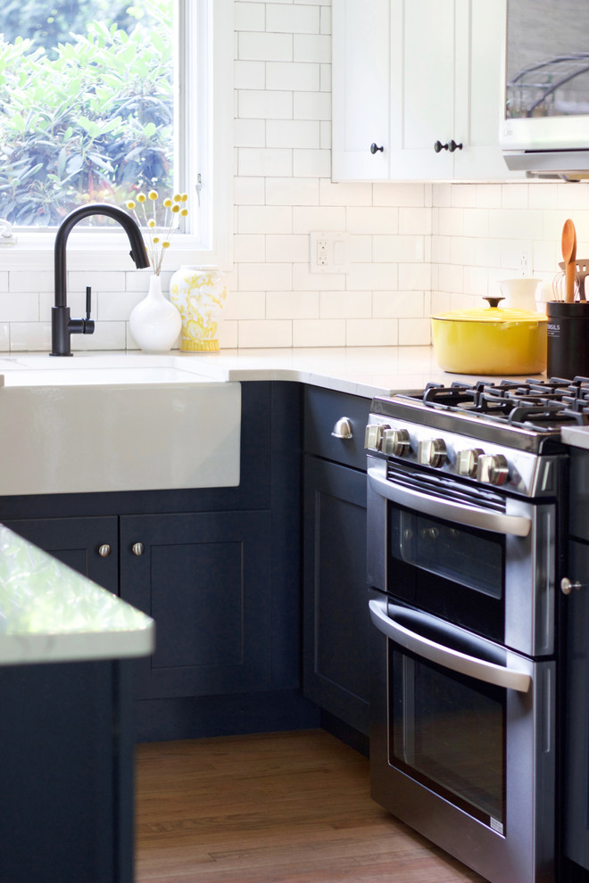 Transitional medium tone wood floor eat-in kitchen photo with a farmhouse sink, shaker cabinets, blue cabinets, quartz countertops, white backsplash, subway tile backsplash, stainless steel appliances, an island and white countertops