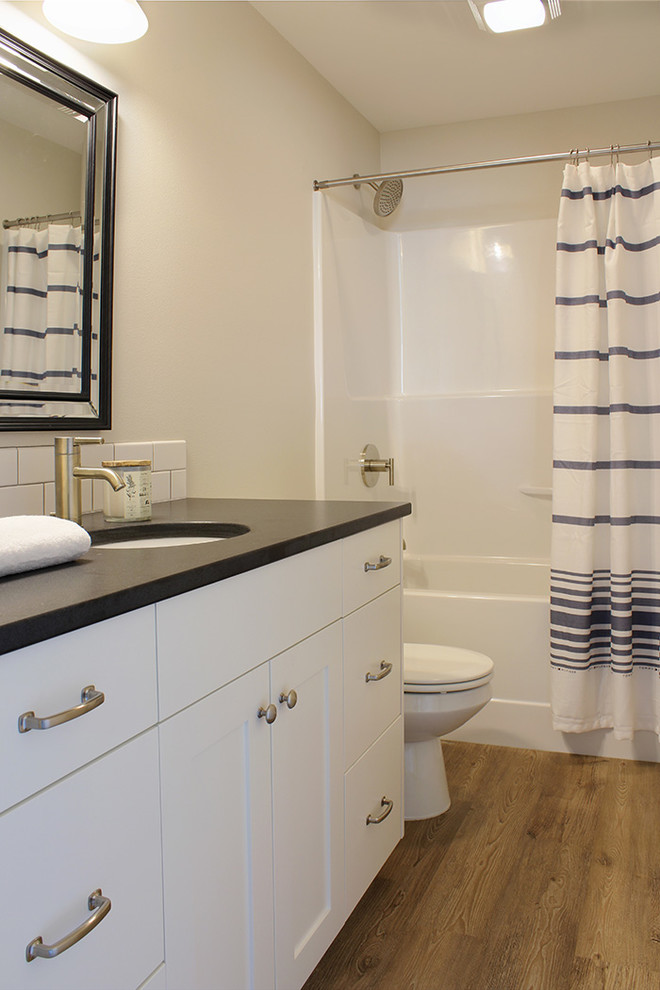Photo of a mid-sized arts and crafts bathroom in Seattle with an undermount sink, shaker cabinets, white cabinets, granite benchtops, an alcove tub, an alcove shower, a one-piece toilet, white tile, subway tile, grey walls and vinyl floors.