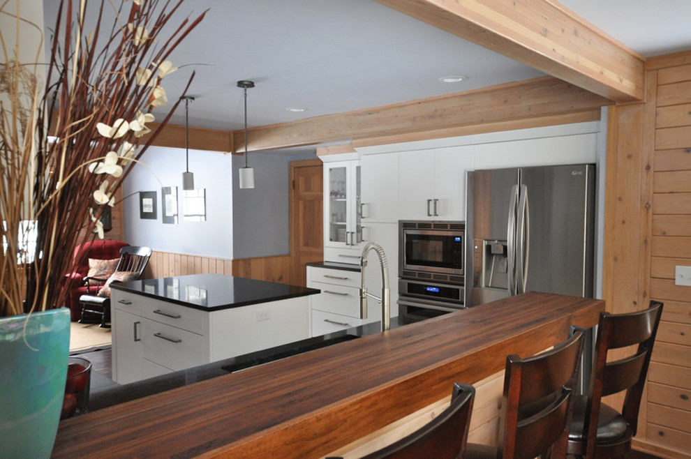 Example of a mid-sized transitional l-shaped dark wood floor eat-in kitchen design in Grand Rapids with an undermount sink, flat-panel cabinets, white cabinets, soapstone countertops, white backsplash, subway tile backsplash, stainless steel appliances and an island