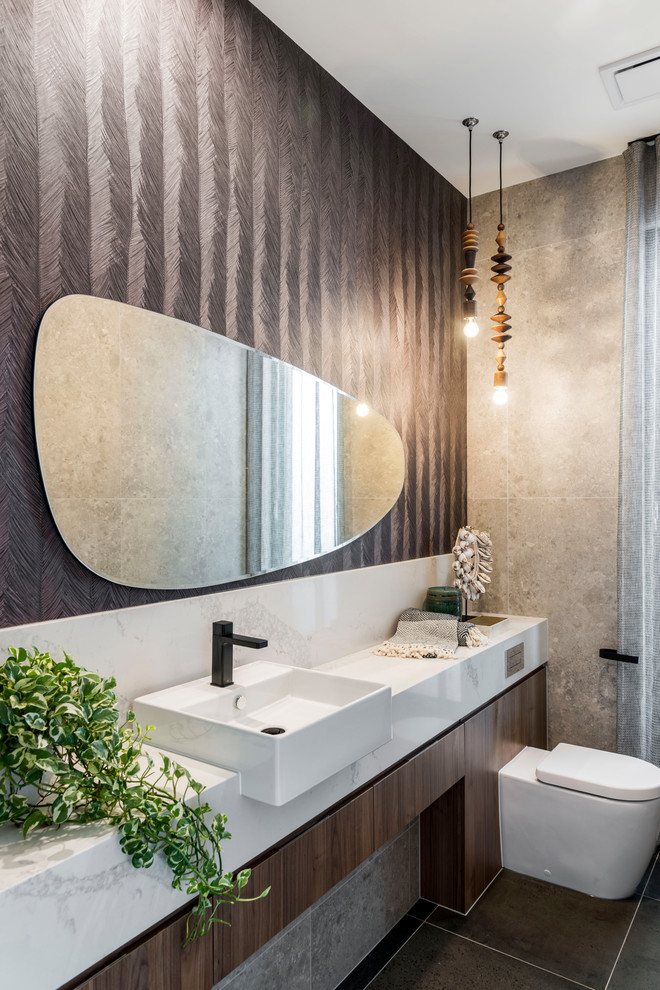 Design ideas for a small contemporary powder room in Gold Coast - Tweed with brown tile, gray tile, brown walls, ceramic floors, brown floor, flat-panel cabinets, medium wood cabinets, a wall-mount toilet, a vessel sink and white benchtops.