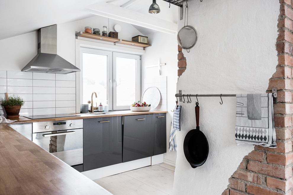 Inspiration for a mid-sized scandinavian l-shaped separate kitchen in Gothenburg with a single-bowl sink, flat-panel cabinets, grey cabinets, wood benchtops, white splashback, porcelain splashback, stainless steel appliances and light hardwood floors.