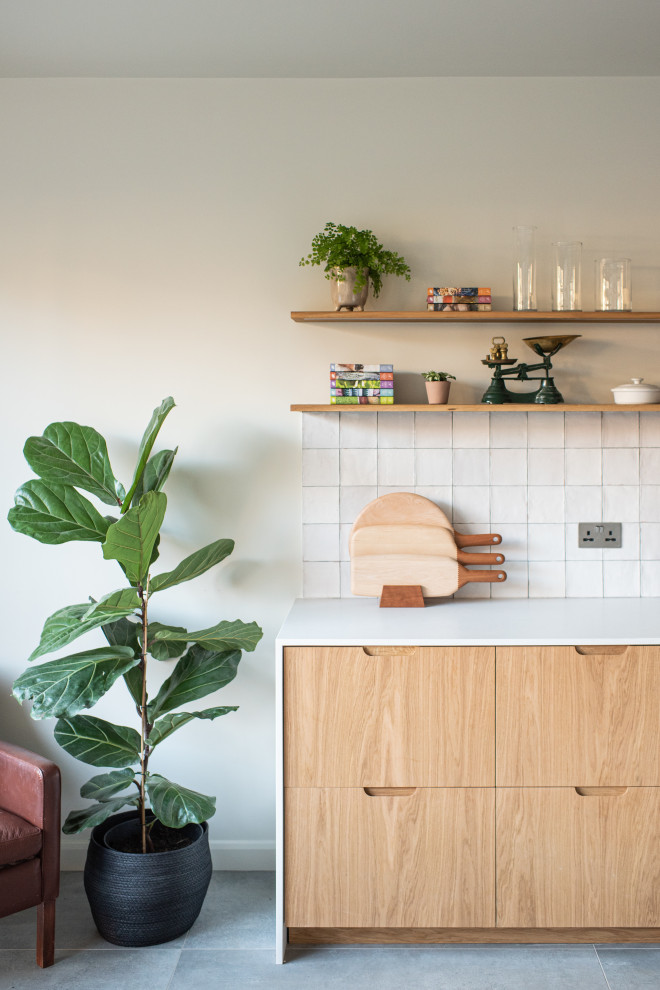 Design ideas for a mid-sized scandinavian single-wall eat-in kitchen in London with a double-bowl sink, flat-panel cabinets, medium wood cabinets, solid surface benchtops, white splashback, ceramic splashback, black appliances, porcelain floors, with island, grey floor and white benchtop.
