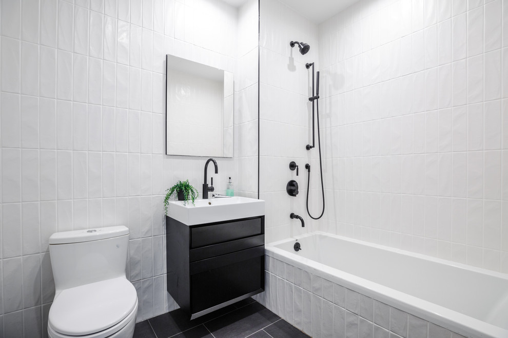 Mid-sized modern bathroom in New York with flat-panel cabinets, black cabinets, a drop-in tub, a one-piece toilet, white tile, porcelain tile, white walls, porcelain floors, an integrated sink, solid surface benchtops, grey floor and white benchtops.
