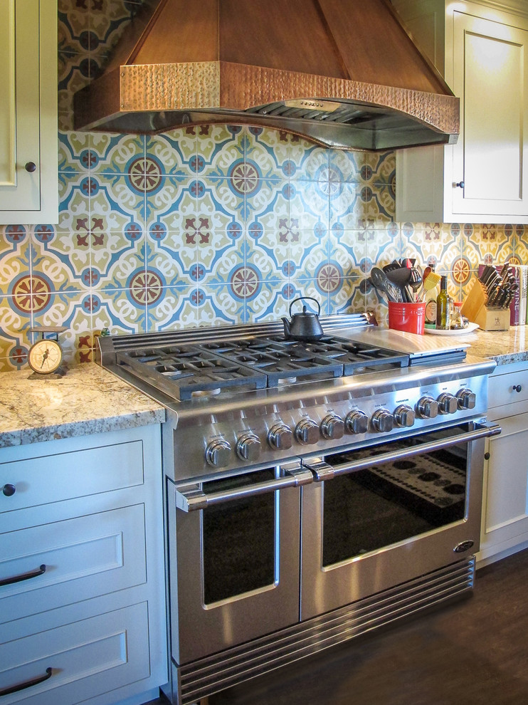 Example of a dark wood floor kitchen design with a farmhouse sink, beaded inset cabinets, white cabinets, multicolored backsplash, ceramic backsplash, stainless steel appliances and an island