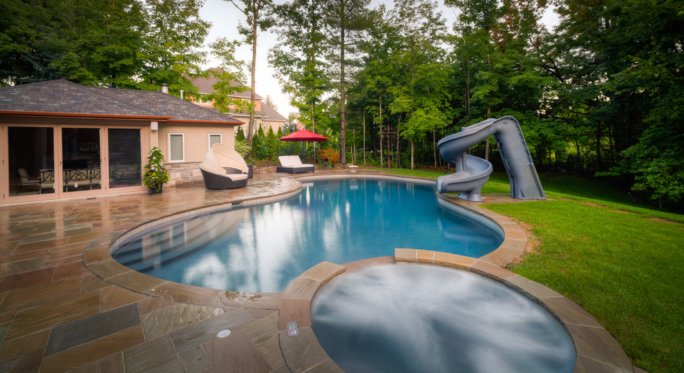 This is an example of a large traditional backyard pool in Other with a water slide and natural stone pavers.