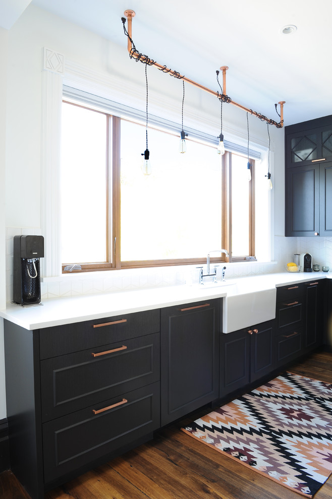 This is an example of a mid-sized eclectic l-shaped open plan kitchen in Vancouver with a farmhouse sink, flat-panel cabinets, black cabinets, quartz benchtops, white splashback, ceramic splashback, stainless steel appliances, medium hardwood floors and with island.