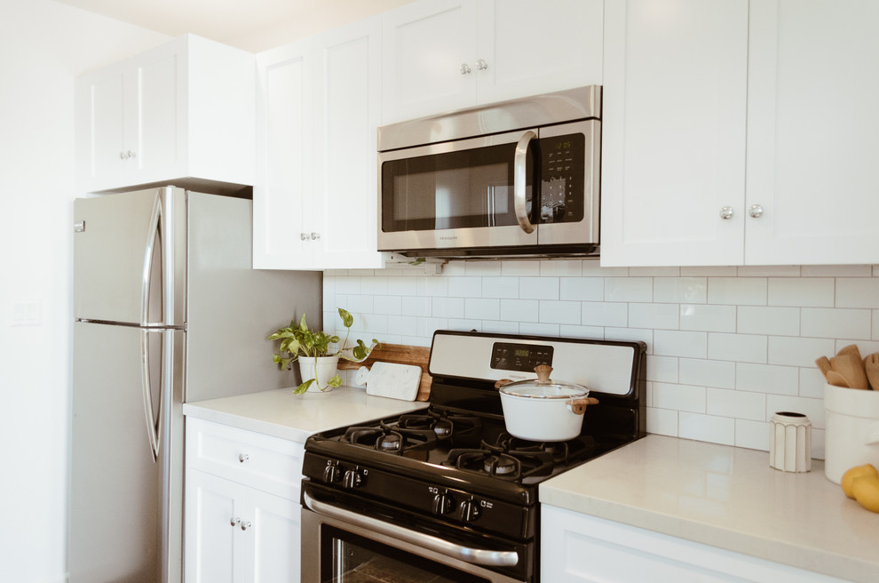 This is an example of a small beach style galley separate kitchen in San Diego with an undermount sink, shaker cabinets, white cabinets, quartz benchtops, white splashback, subway tile splashback, stainless steel appliances, ceramic floors and no island.