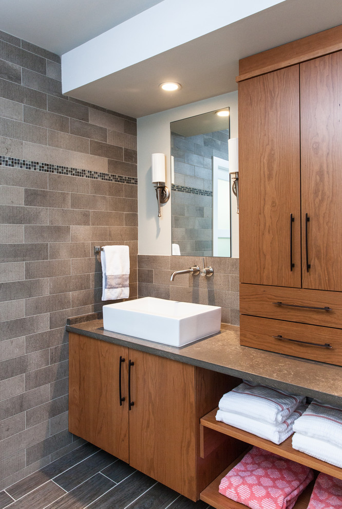 This is an example of a mid-sized eclectic master bathroom in Detroit with flat-panel cabinets, medium wood cabinets, an undermount tub, an open shower, a one-piece toilet, gray tile, stone tile, grey walls, porcelain floors, a vessel sink and quartzite benchtops.