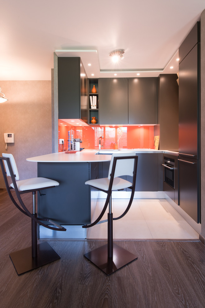 Mid-sized contemporary u-shaped eat-in kitchen in Paris with an integrated sink, beaded inset cabinets, brown cabinets, solid surface benchtops, orange splashback, glass tile splashback, panelled appliances, ceramic floors and a peninsula.