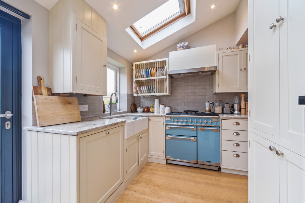 Inspiration for a transitional l-shaped kitchen in London with a farmhouse sink, shaker cabinets, beige cabinets, grey splashback, coloured appliances, medium hardwood floors, no island, brown floor, grey benchtop and vaulted.