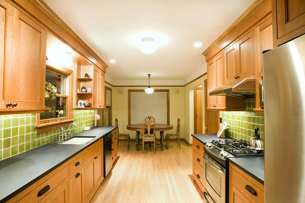 Photo of an arts and crafts galley eat-in kitchen in Seattle with stainless steel appliances, an undermount sink, recessed-panel cabinets, medium wood cabinets, green splashback, glass tile splashback and no island.