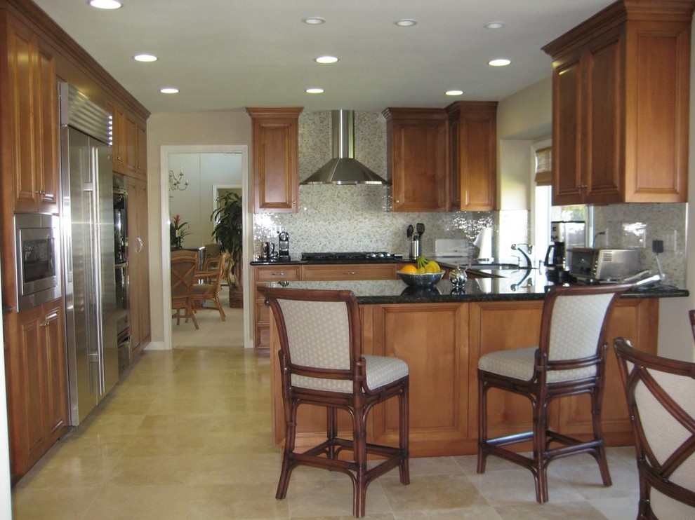 Example of a mid-sized transitional u-shaped limestone floor eat-in kitchen design in Orange County with raised-panel cabinets, medium tone wood cabinets, granite countertops, beige backsplash, stone slab backsplash, stainless steel appliances and a peninsula