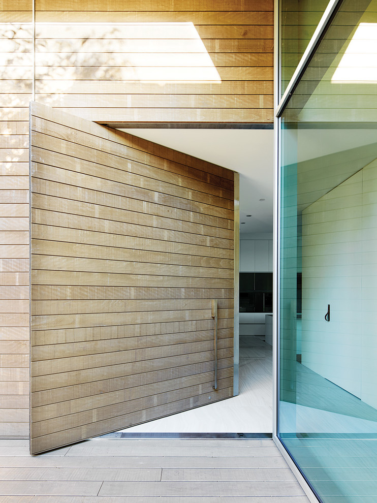 This is an example of an expansive modern front door in Vancouver with a medium wood front door, a pivot front door, white walls and porcelain floors.