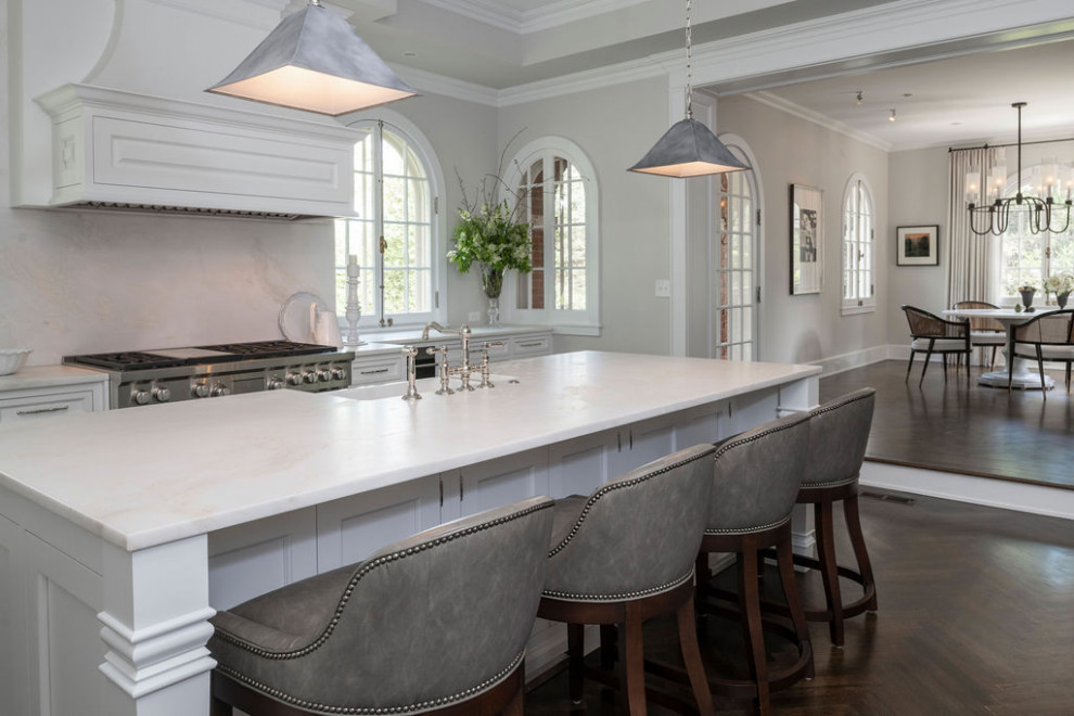 Klassisk inredning av ett vit vitt kök och matrum, med en rustik diskho, skåp i shakerstil, vita skåp, marmorbänkskiva, vitt stänkskydd, stänkskydd i marmor, rostfria vitvaror, mörkt trägolv, en köksö och brunt golv