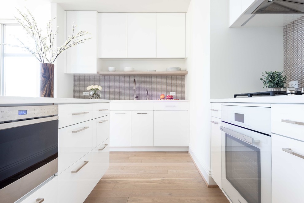 This is an example of a large contemporary u-shaped eat-in kitchen in DC Metro with an undermount sink, flat-panel cabinets, white cabinets, solid surface benchtops, metallic splashback, metal splashback, panelled appliances, light hardwood floors, with island, beige floor and white benchtop.