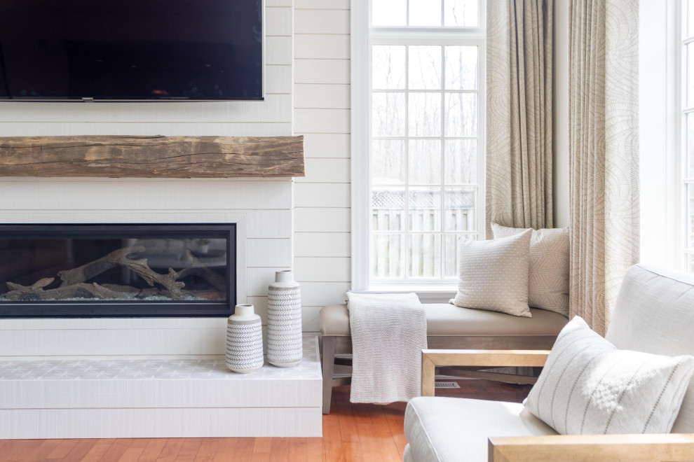 This is an example of a large transitional open concept family room in Toronto with beige walls, medium hardwood floors, a standard fireplace, a wood fireplace surround, a wall-mounted tv and orange floor.