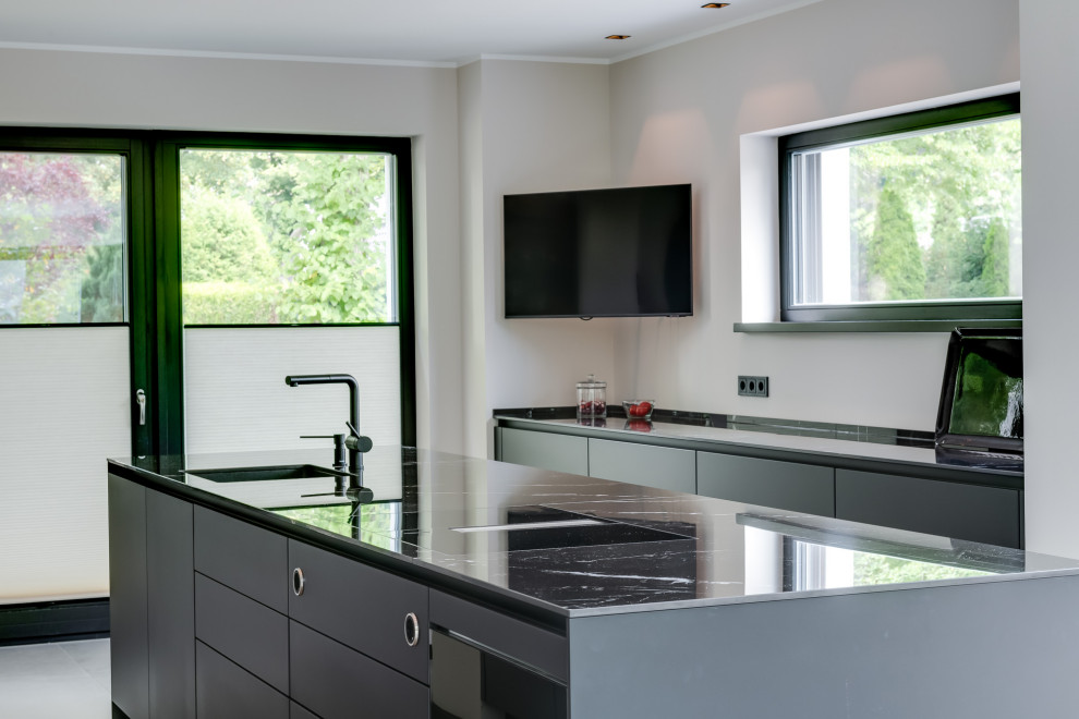 Photo of an expansive modern galley open plan kitchen in Hamburg with an integrated sink, flat-panel cabinets, black cabinets, quartz benchtops, black splashback, ceramic splashback, black appliances, ceramic floors, with island, grey floor, black benchtop and recessed.