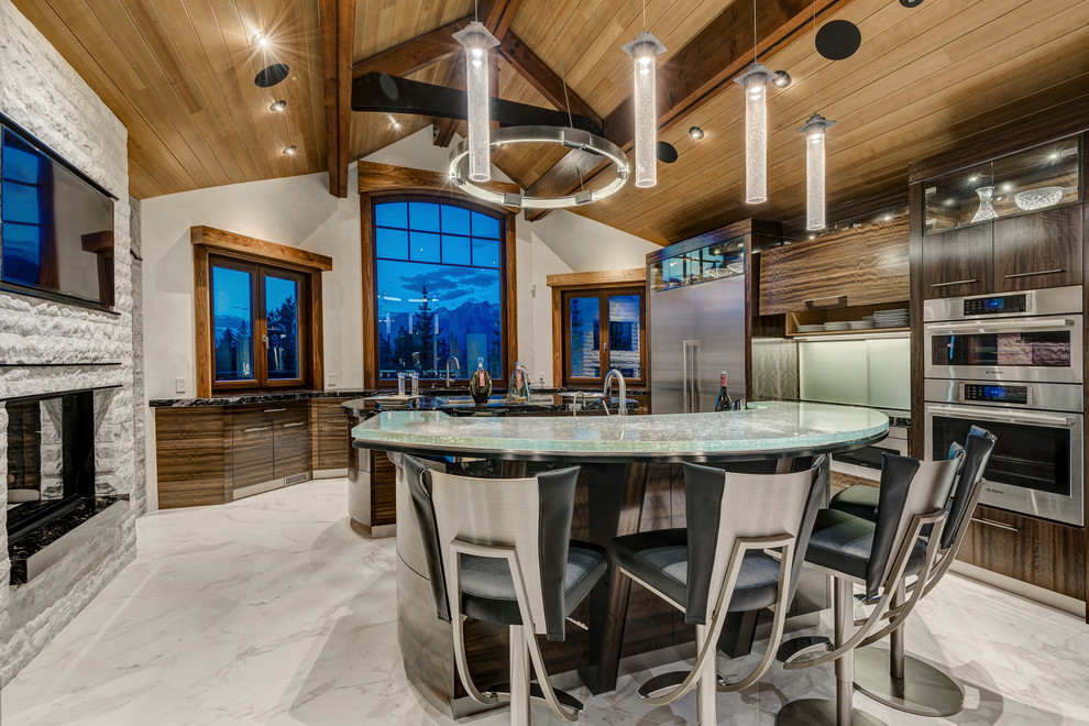 Photo of an expansive contemporary u-shaped kitchen with a farmhouse sink, flat-panel cabinets, brown cabinets, glass benchtops, stainless steel appliances, marble floors, multiple islands and white floor.