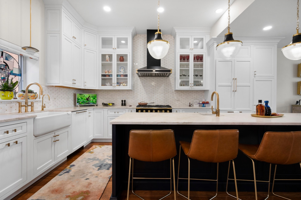 This is an example of a large contemporary l-shaped kitchen pantry in Chicago with a farmhouse sink, shaker cabinets, white cabinets, quartzite benchtops, beige splashback, mosaic tile splashback, black appliances, dark hardwood floors, with island and beige benchtop.