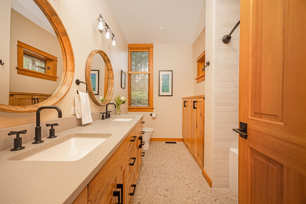 Example of a mid-sized mountain style kids' gray tile and porcelain tile terrazzo floor, gray floor and double-sink alcove bathtub design with shaker cabinets, medium tone wood cabinets, a one-piece toilet, beige walls, an undermount sink, quartz countertops, gray countertops, a niche and a freestanding vanity