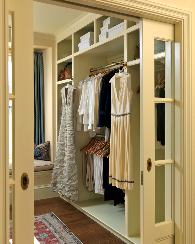 This is an example of a traditional gender-neutral dressing room in Boston with open cabinets, medium hardwood floors, beige cabinets and brown floor.