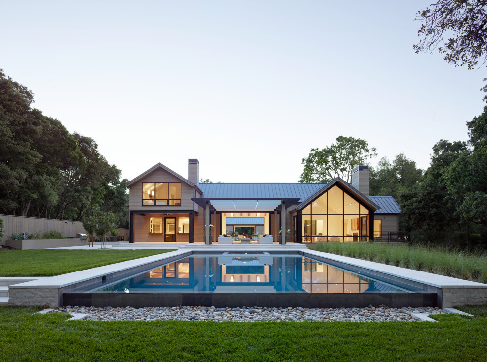 Modelo de piscina infinita campestre grande rectangular en patio trasero con paisajismo de piscina y adoquines de piedra natural