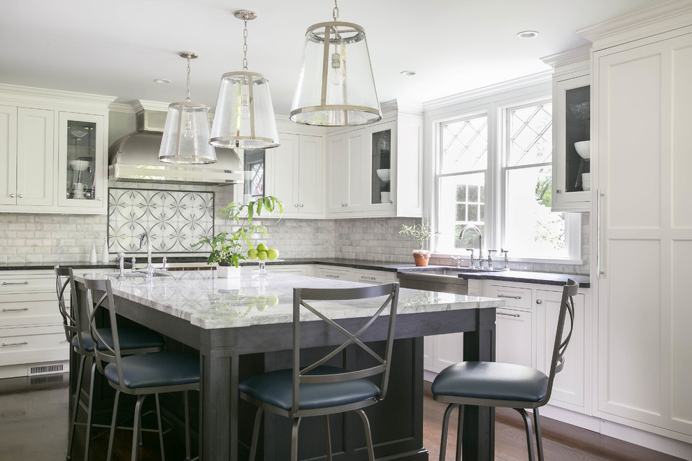 Example of a large transitional l-shaped dark wood floor enclosed kitchen design in New York with a farmhouse sink, recessed-panel cabinets, white cabinets, quartzite countertops, gray backsplash, stone tile backsplash and an island