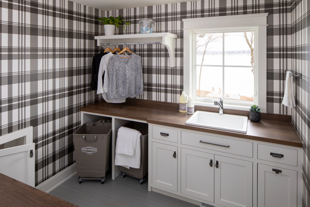 Example of a beach style galley gray floor and wallpaper dedicated laundry room design in Minneapolis with a drop-in sink, shaker cabinets, white cabinets, wood countertops, multicolored walls and brown countertops