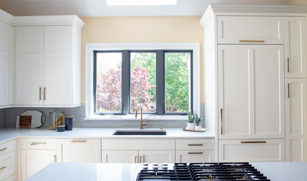 Example of a large transitional u-shaped medium tone wood floor kitchen design with an undermount sink, white cabinets, quartz countertops, gray backsplash, glass tile backsplash, stainless steel appliances, an island and white countertops
