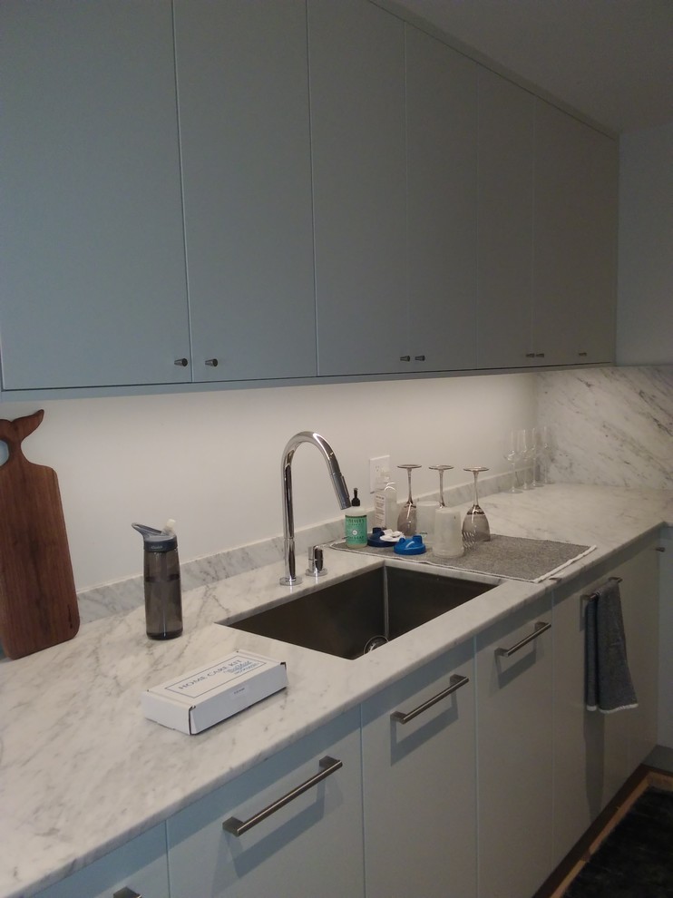 Small modern u-shaped kitchen in Chicago with an undermount sink, flat-panel cabinets, white cabinets, marble benchtops, stone slab splashback, black appliances, medium hardwood floors, white floor and white benchtop.