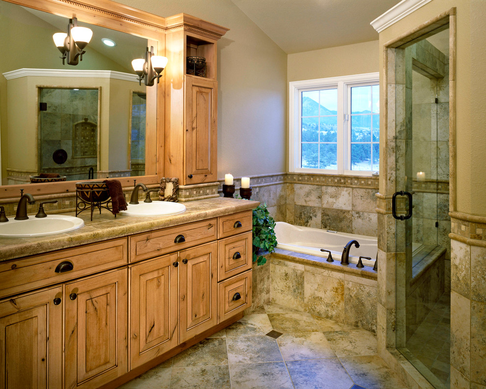 This is an example of a country master bathroom in Denver with a drop-in sink, light wood cabinets, a corner tub, a corner shower, beige tile and beige walls.