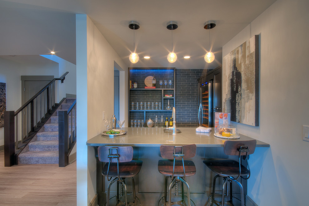 Inspiration for a mid-sized traditional l-shaped seated home bar in Calgary with open cabinets, an undermount sink, grey cabinets, solid surface benchtops, grey splashback, subway tile splashback and vinyl floors.