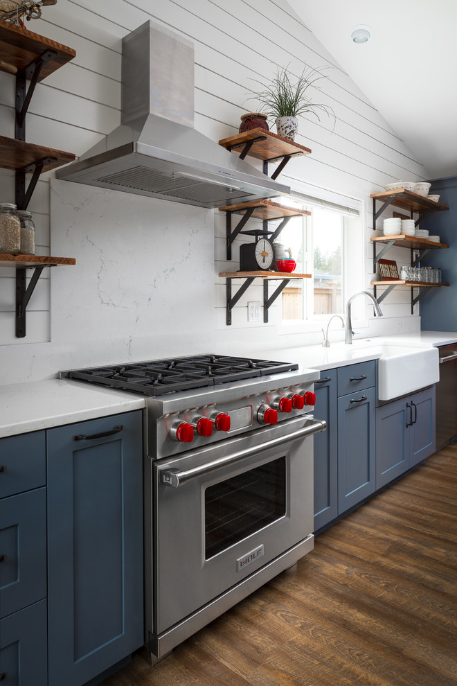 This is an example of a mid-sized country single-wall kitchen pantry in Portland with a farmhouse sink, shaker cabinets, grey cabinets, quartz benchtops, stainless steel appliances, medium hardwood floors, with island, brown floor, white splashback and stone slab splashback.