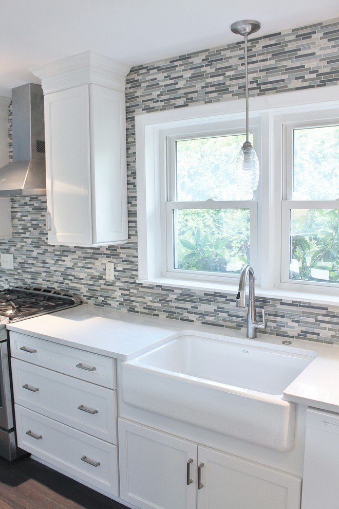 This is an example of a mid-sized transitional l-shaped eat-in kitchen in Philadelphia with a farmhouse sink, shaker cabinets, white cabinets, quartz benchtops, blue splashback, mosaic tile splashback, stainless steel appliances, vinyl floors, with island and brown floor.