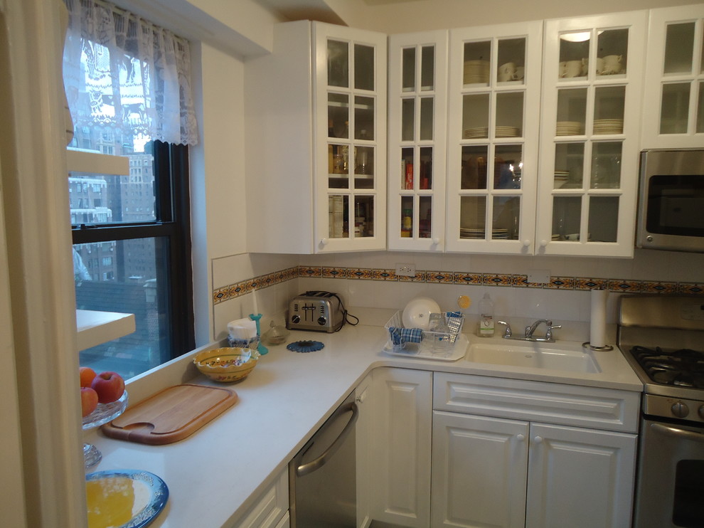 Photo of a traditional u-shaped eat-in kitchen in New York with an undermount sink, raised-panel cabinets, white cabinets, recycled glass benchtops, white splashback, cement tile splashback and stainless steel appliances.