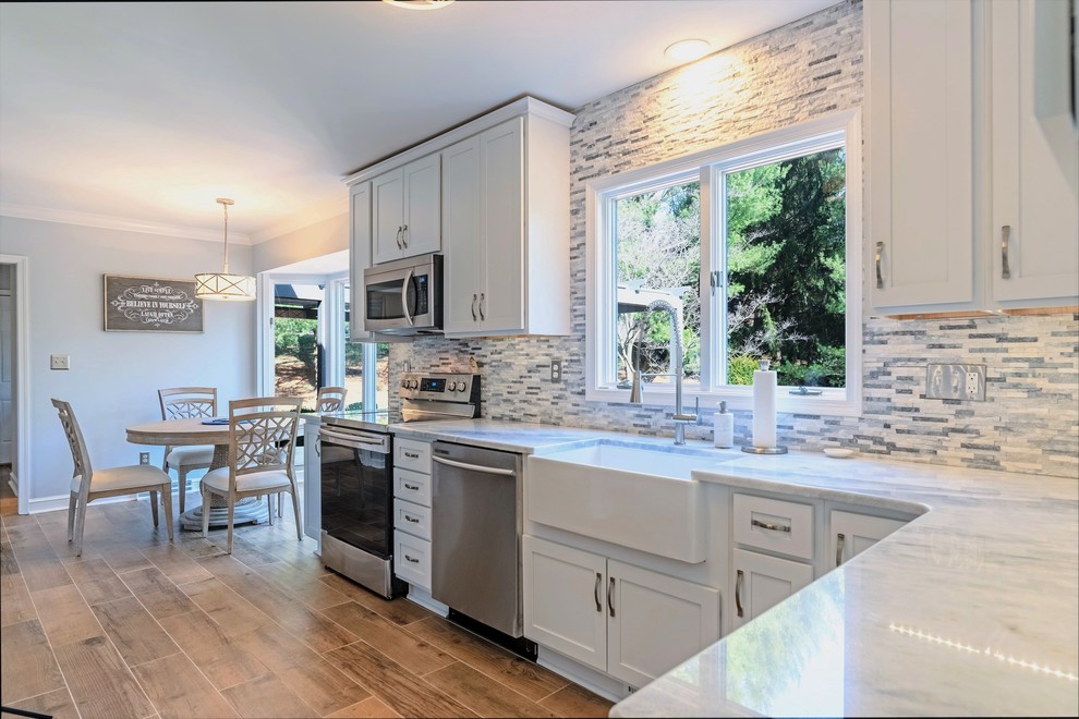 Example of a large transitional l-shaped ceramic tile and brown floor eat-in kitchen design in Baltimore with a farmhouse sink, shaker cabinets, white cabinets, granite countertops, gray backsplash, stone tile backsplash, stainless steel appliances, no island and white countertops