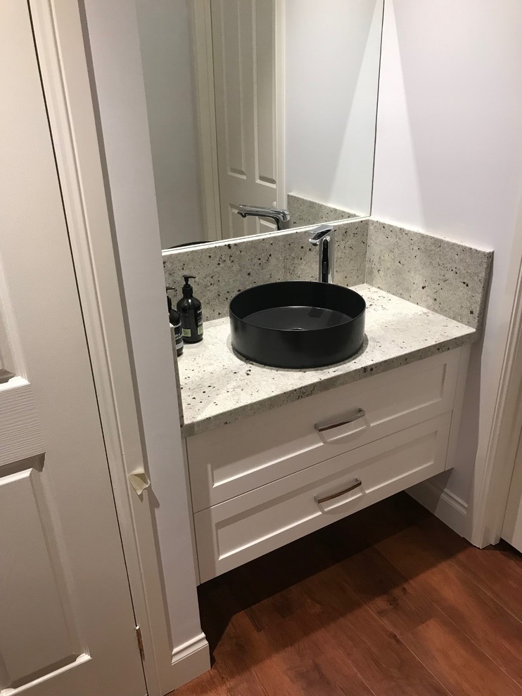 This is an example of a small traditional powder room in Melbourne with shaker cabinets, white cabinets, a two-piece toilet, white walls, medium hardwood floors, a vessel sink, granite benchtops and white benchtops.
