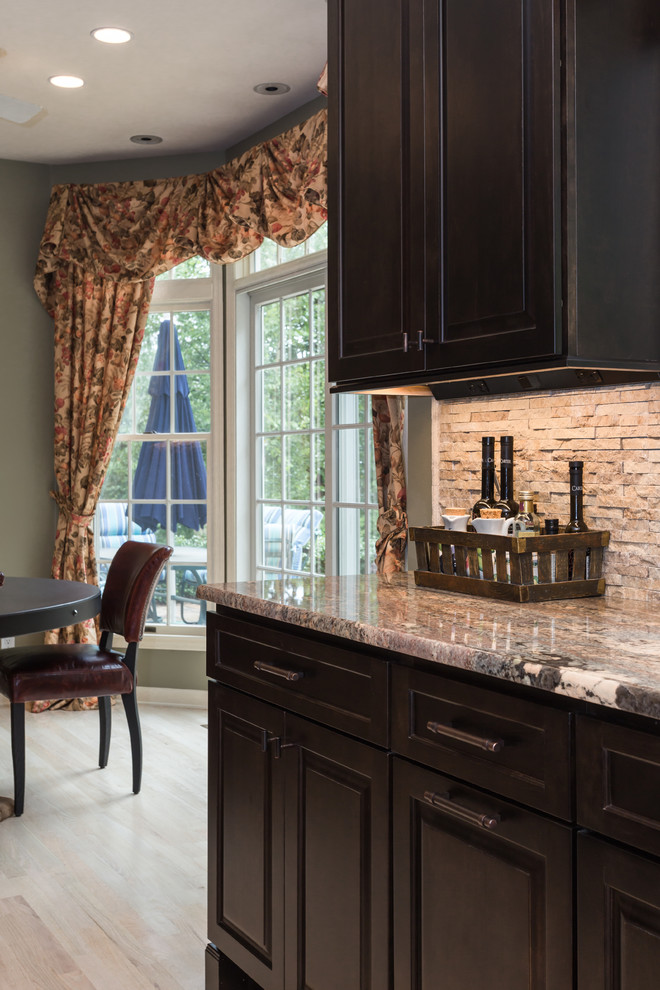 Large tuscan u-shaped light wood floor eat-in kitchen photo in New York with a single-bowl sink, raised-panel cabinets, dark wood cabinets, granite countertops, beige backsplash, stone tile backsplash, stainless steel appliances and an island