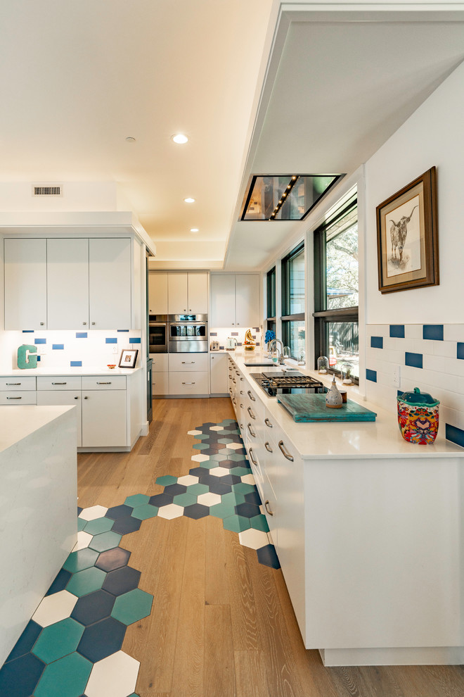 Large traditional single-wall open plan kitchen in Austin with a drop-in sink, flat-panel cabinets, white cabinets, quartz benchtops, blue splashback, subway tile splashback, stainless steel appliances, porcelain floors, with island, blue floor and white benchtop.