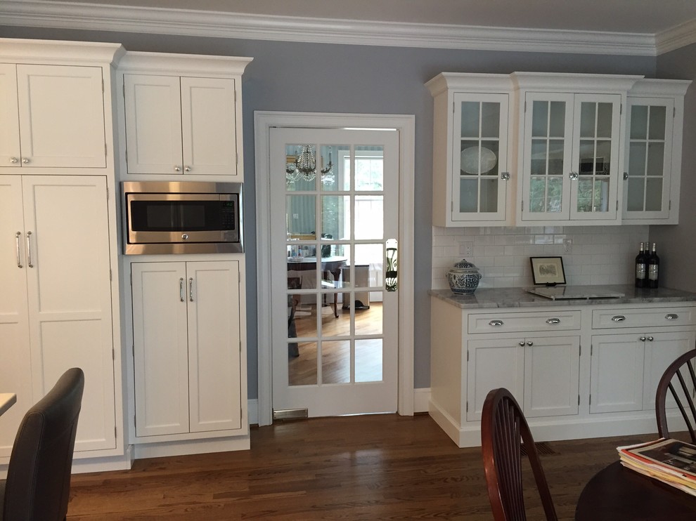 Mid-sized transitional l-shaped medium tone wood floor eat-in kitchen photo in Bridgeport with an undermount sink, shaker cabinets, white cabinets, solid surface countertops, white backsplash, subway tile backsplash, stainless steel appliances and an island